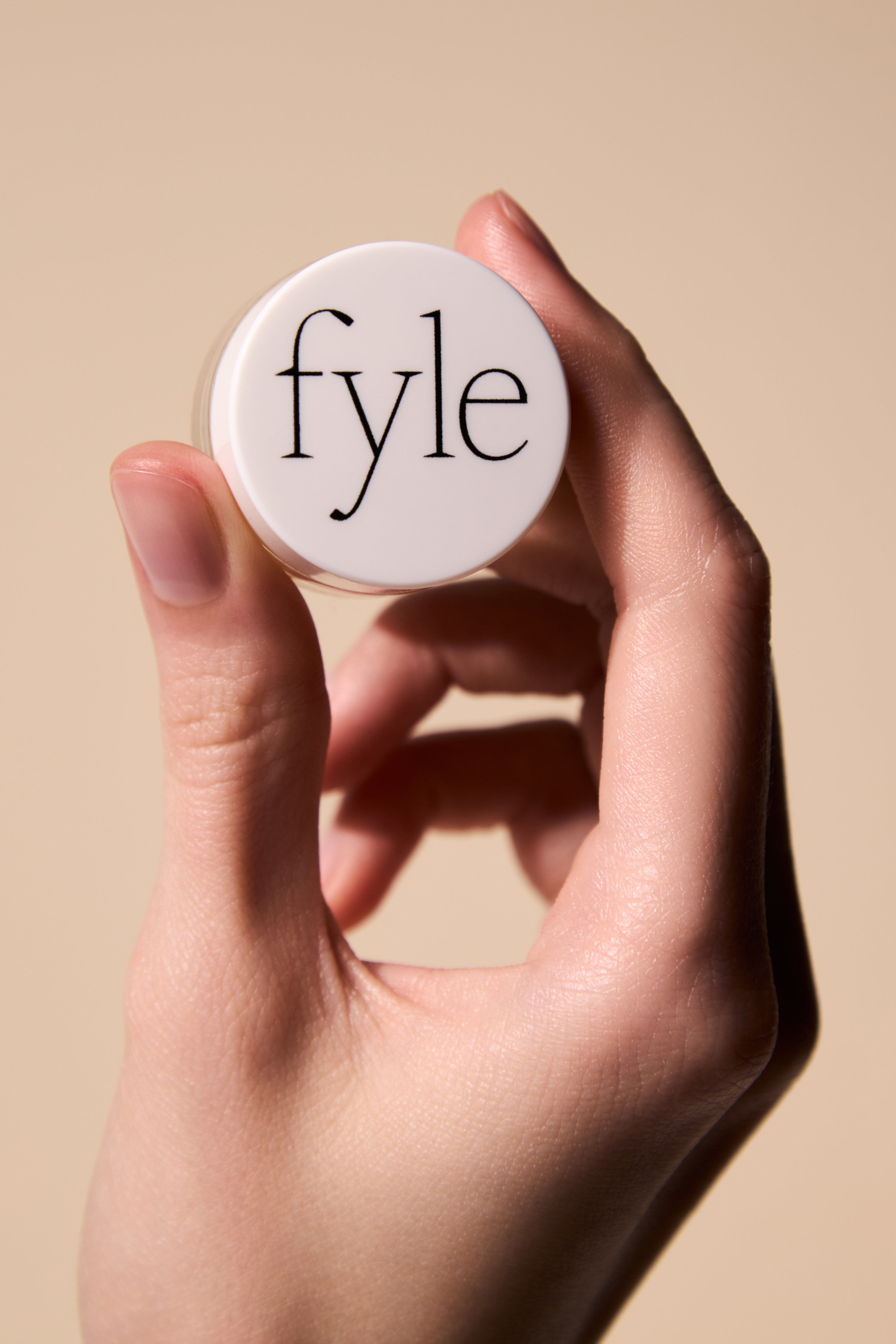 Hand holding the Fyle Cuticle Sealing Balm, showing the clean white jar with logo.
